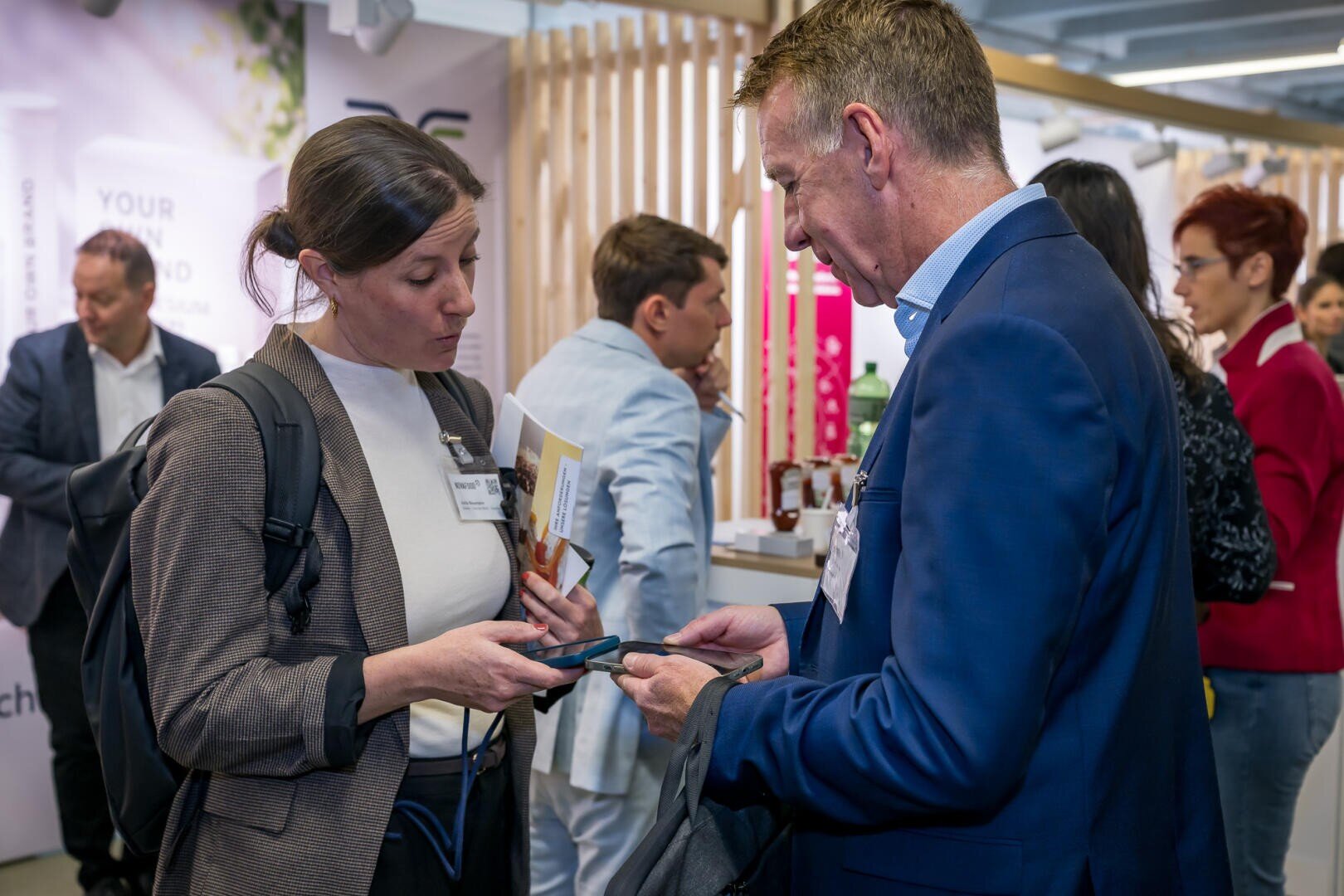 Eine Frau und ein Mann in Geschäftskleidung tauschen auf einer Konferenz ihre Kontaktdaten aus, indem sie ihre Smartphones aneinanderhalten.