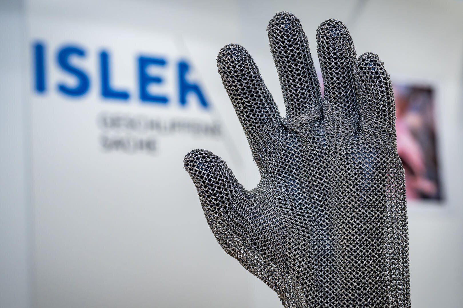 Ein schützender Handschuh aus Metallkettengeflecht, der vor einem unscharfen Hintergrund gehalten wird, mit dem Markennamen ISLER.