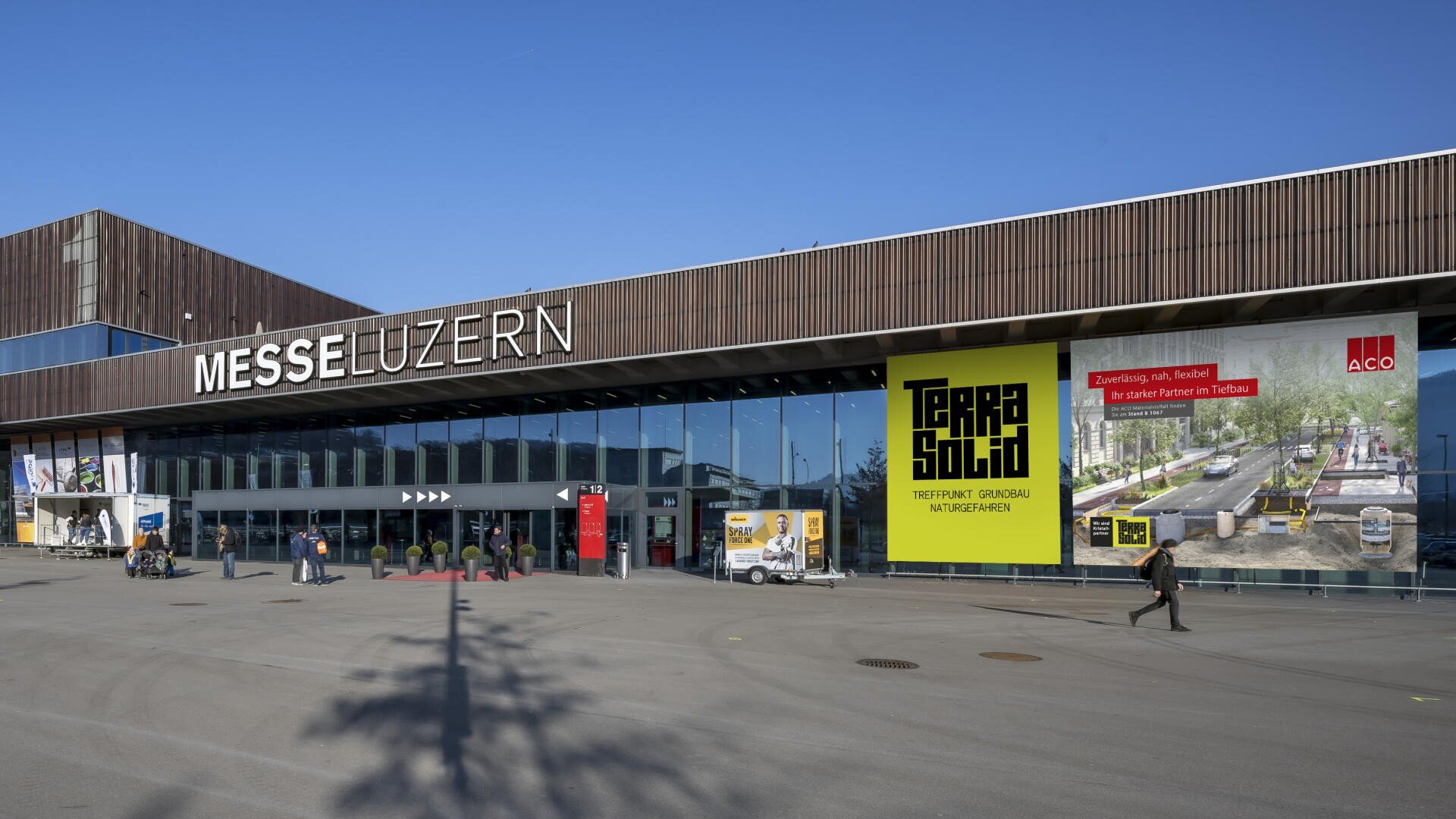 Die Aussenansicht der Messe Luzern mit grossen Glasfenstern, moderner brauner Verkleidung, blauem Himmel und einer gelben Terra Solid Werbung.