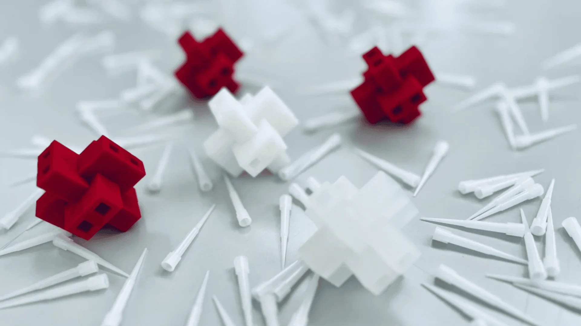 Rote und weiße ineinander greifende Puzzleteile aus Kunststoff sind auf einer Oberfläche zwischen vielen kleinen weißen zylindrischen Stiften verstreut und bilden so ein verspieltes und abstraktes Arrangement.