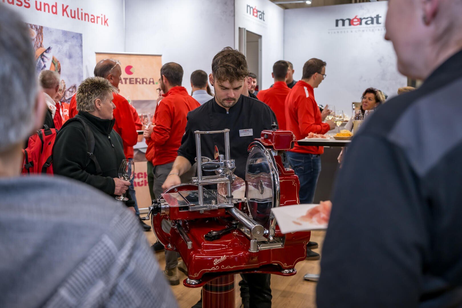 Ein Koch schneidet an einem roten Berkel-Aufschnittgerät an einem gut besuchten Messestand Wurstwaren in Scheiben.