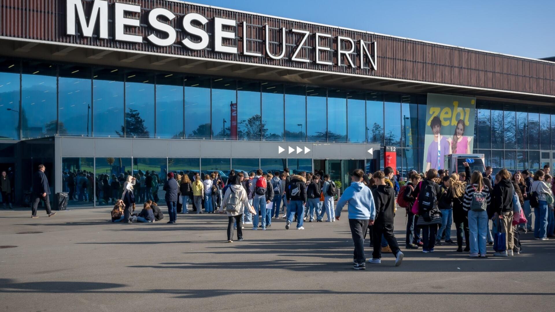 Vor dem Kongresszentrum der Messe Luzern versammelt sich eine grosse Menschenmenge, die bei strahlend blauem Himmel auf dem Trottoir vor dem Glaseingang steht.