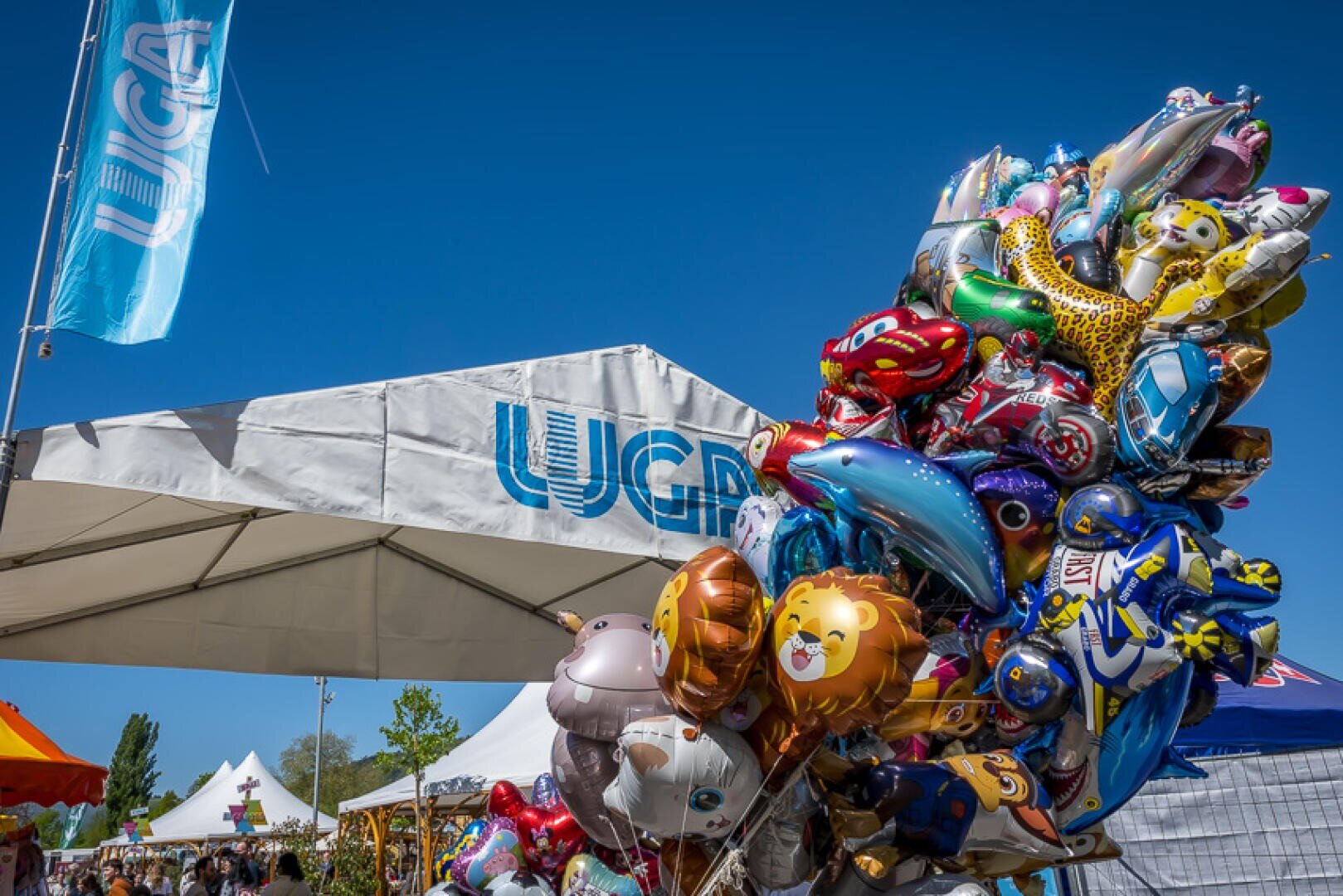 Eine Ansammlung von bunten Tier- und Cartoon-Ballons bei einem Fest im Freien, mit einem weißen Zelt und einem blauen UGA-Banner im Hintergrund unter einem klaren blauen Himmel.
