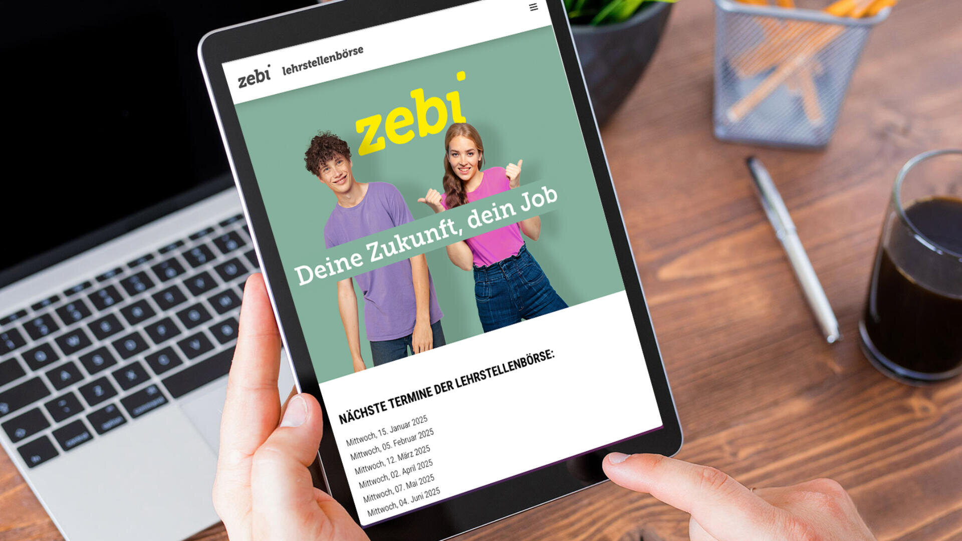 Eine Person hält ein Tablet in der Hand, auf dem eine Website mit zwei lächelnden jungen Menschen und dem Text „zebi – Deine Zukunft, dein Job“ angezeigt wird. Darunter finden sich Informationen zu bevorstehenden Terminen von Jobmessen auf Deutsch. Auf dem Tisch stehen ein Kaffee- und ein Stifthalter.